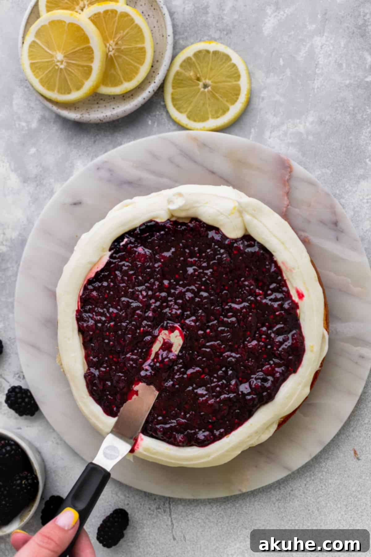 Zesty Lemon Blackberry Delight 11 Spreading homemade blackberry jam evenly over a frosted cake layer.