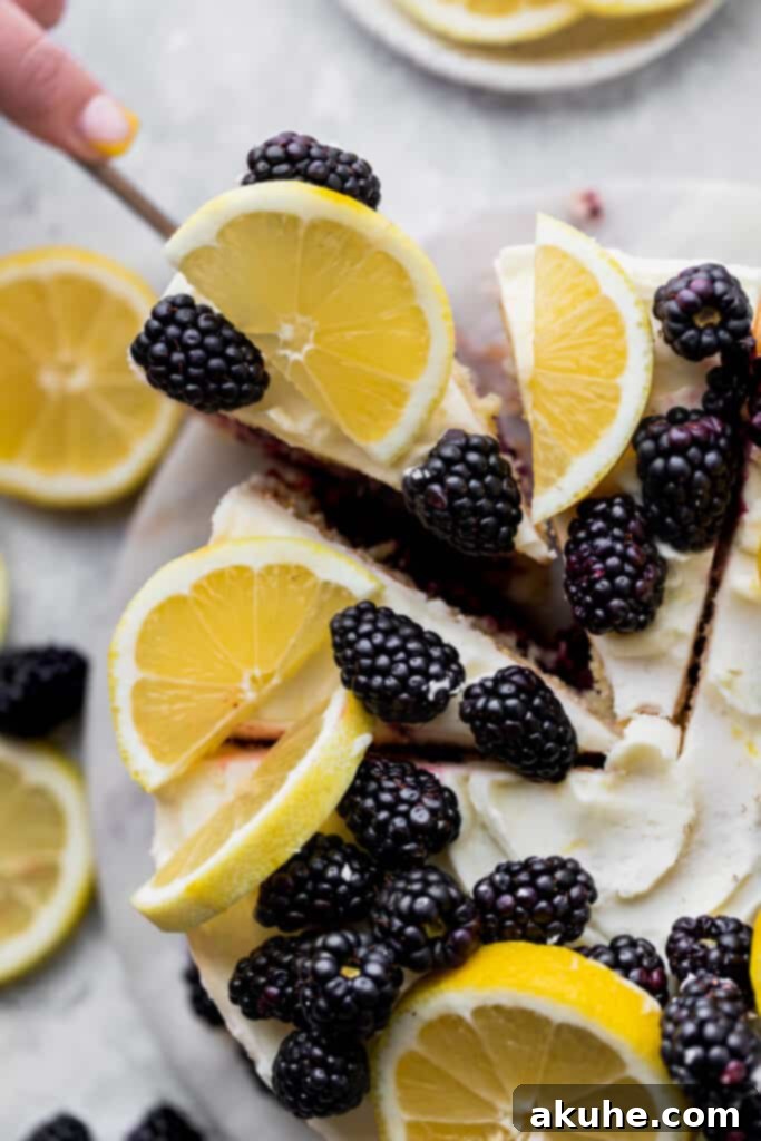 Zesty Lemon Blackberry Delight 13 Top-down view of a Lemon Blackberry Cake on a cutting board, with a slice being pulled out.