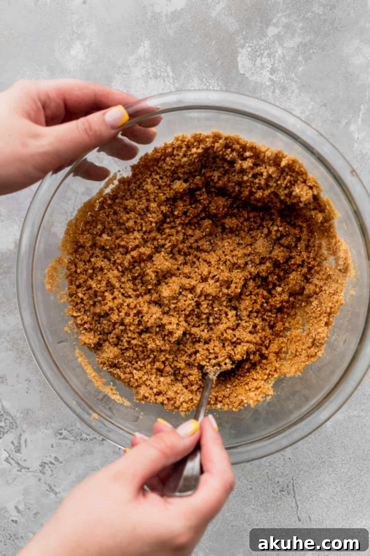 Graham cracker crust crumbs mixed with butter and sugar in a glass bowl.