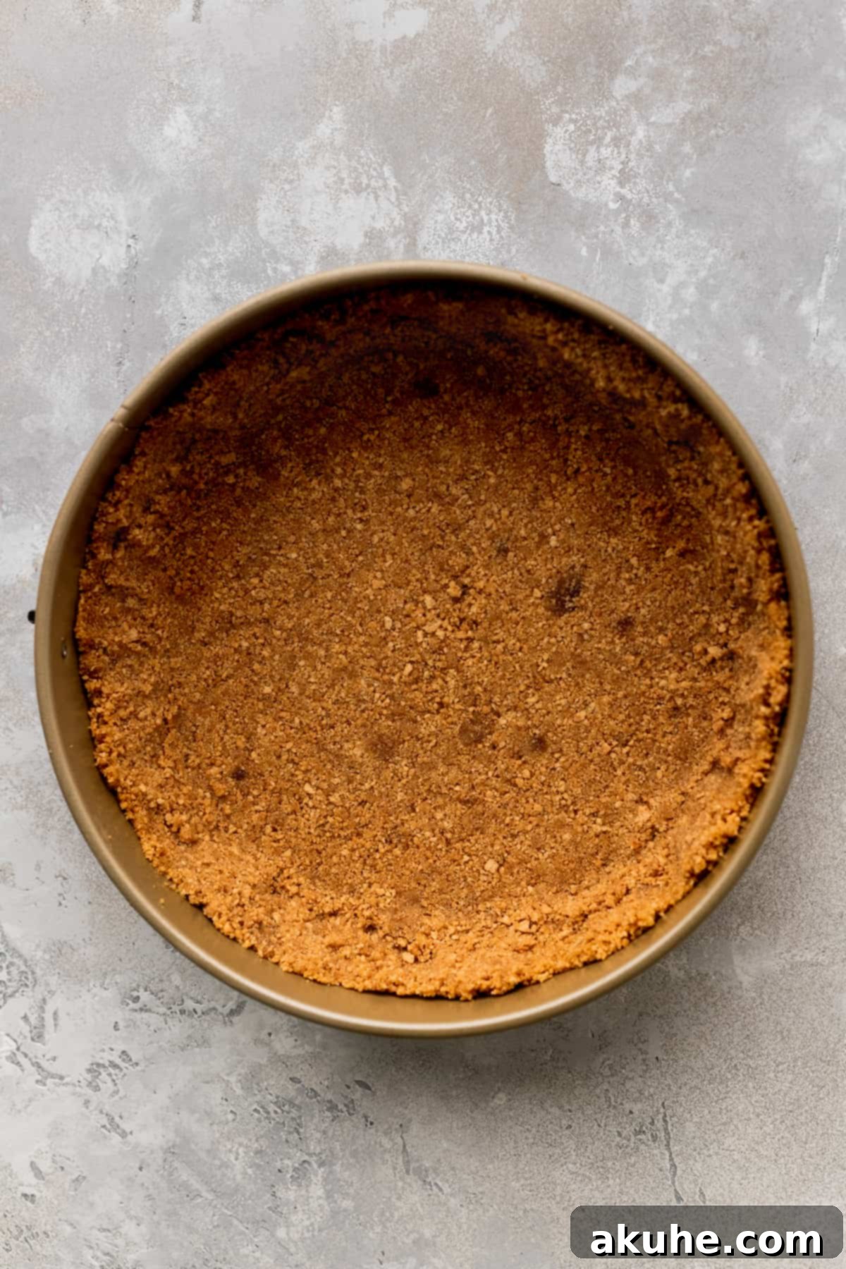 Compacted graham cracker crust pressed into a springform pan, ready for baking.