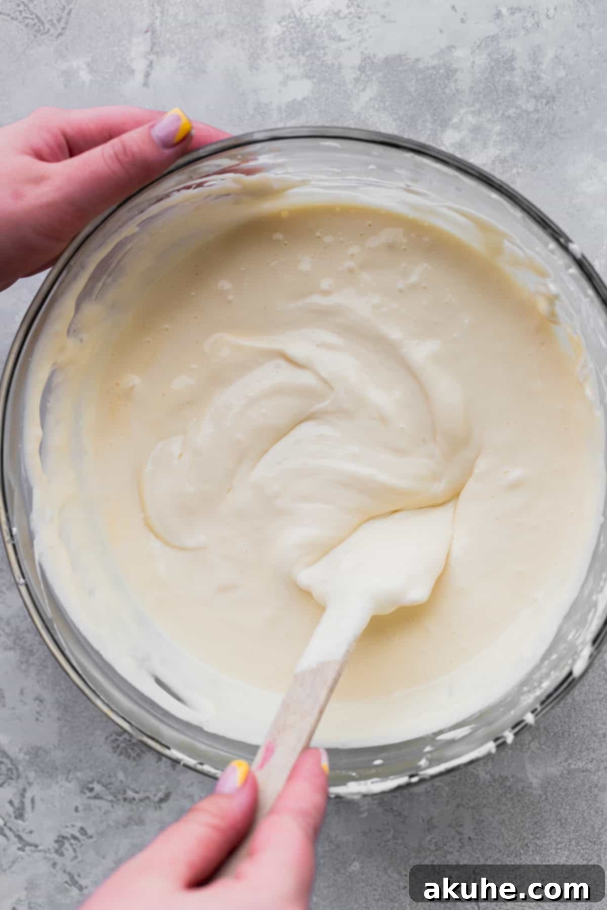 Smooth cheesecake batter being gently stirred with a rubber spatula before baking.