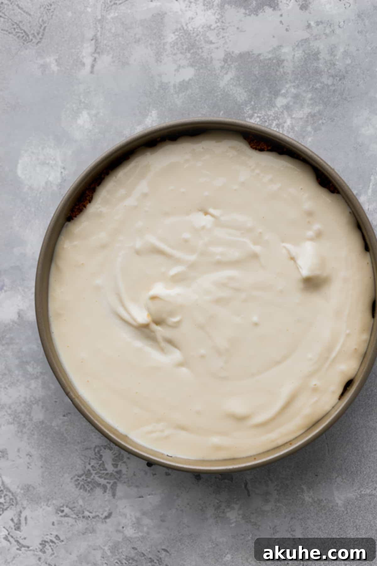 Unbaked cheesecake batter perfectly poured into a springform pan over the graham cracker crust.