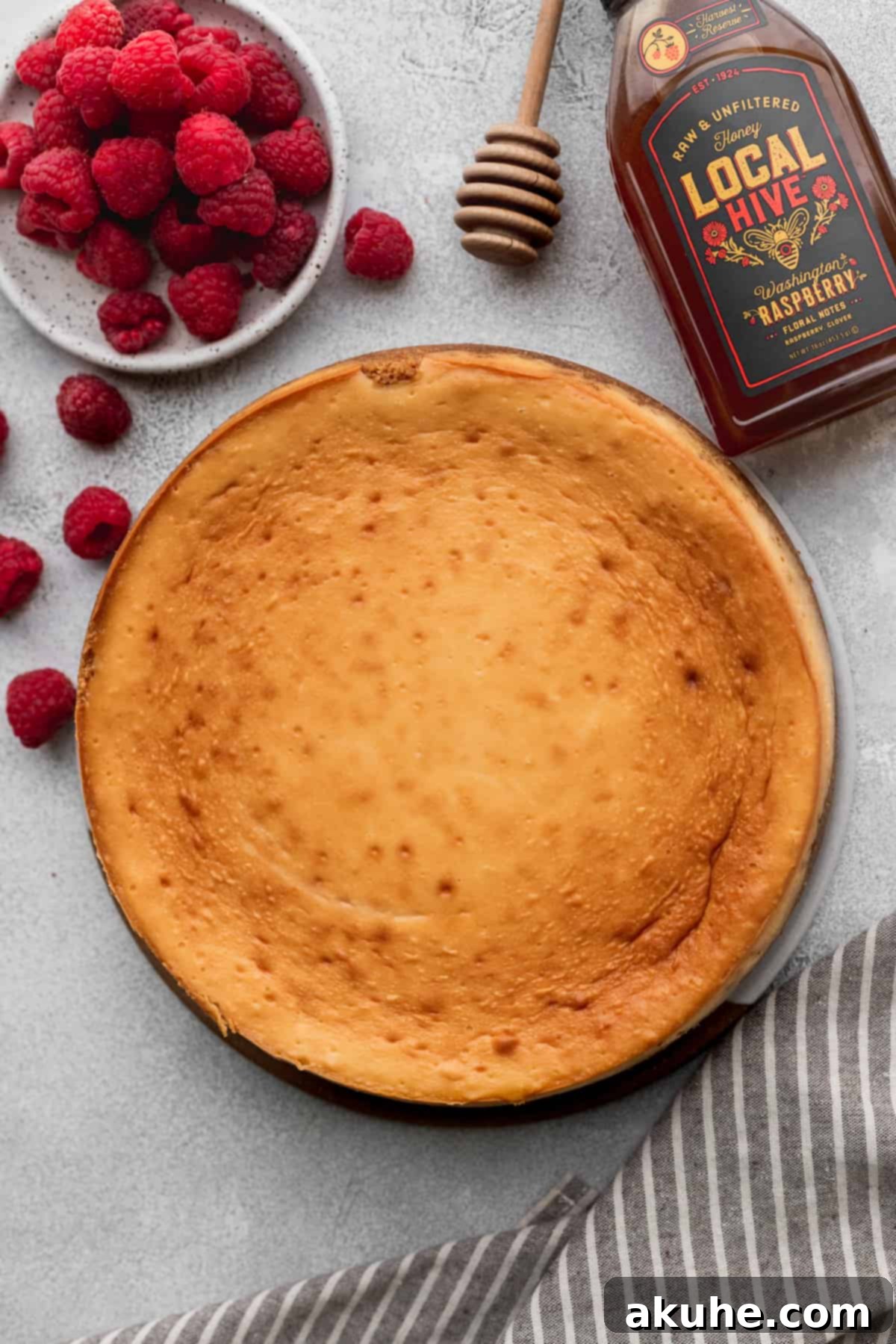 A beautifully baked honey cheesecake on a serving platter, garnished with fresh raspberries.