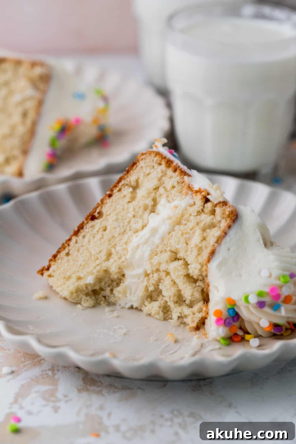 Vanilla Bean Mini Cakes 2 A perfectly sliced mini vanilla cake on a plate, revealing its two layers and creamy frosting. A bite has been taken from the slice.