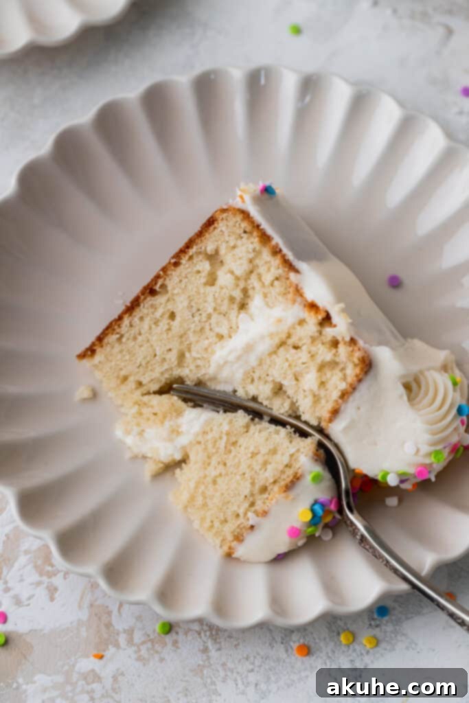 Vanilla Bean Mini Cakes 11 A close-up of a single slice of mini vanilla cake on a plate, with a fork gently inserted into its fluffy layers.