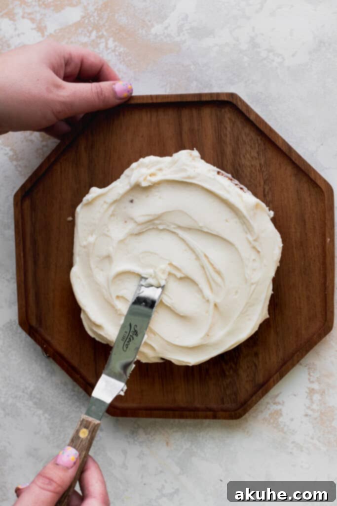 Vanilla Bean Mini Cakes 8 A hand using an offset spatula to smooth the final layer of cream cheese frosting over the top of a mini vanilla cake.