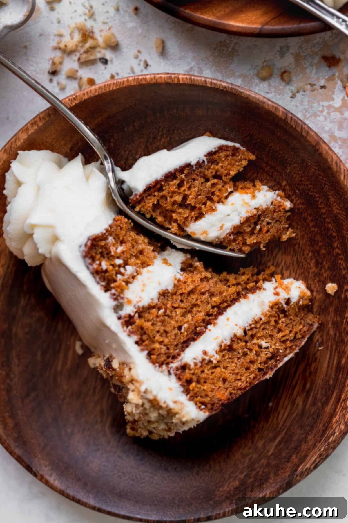 A single slice of mini carrot cake on a wooden plate with a fork, showing multiple layers.