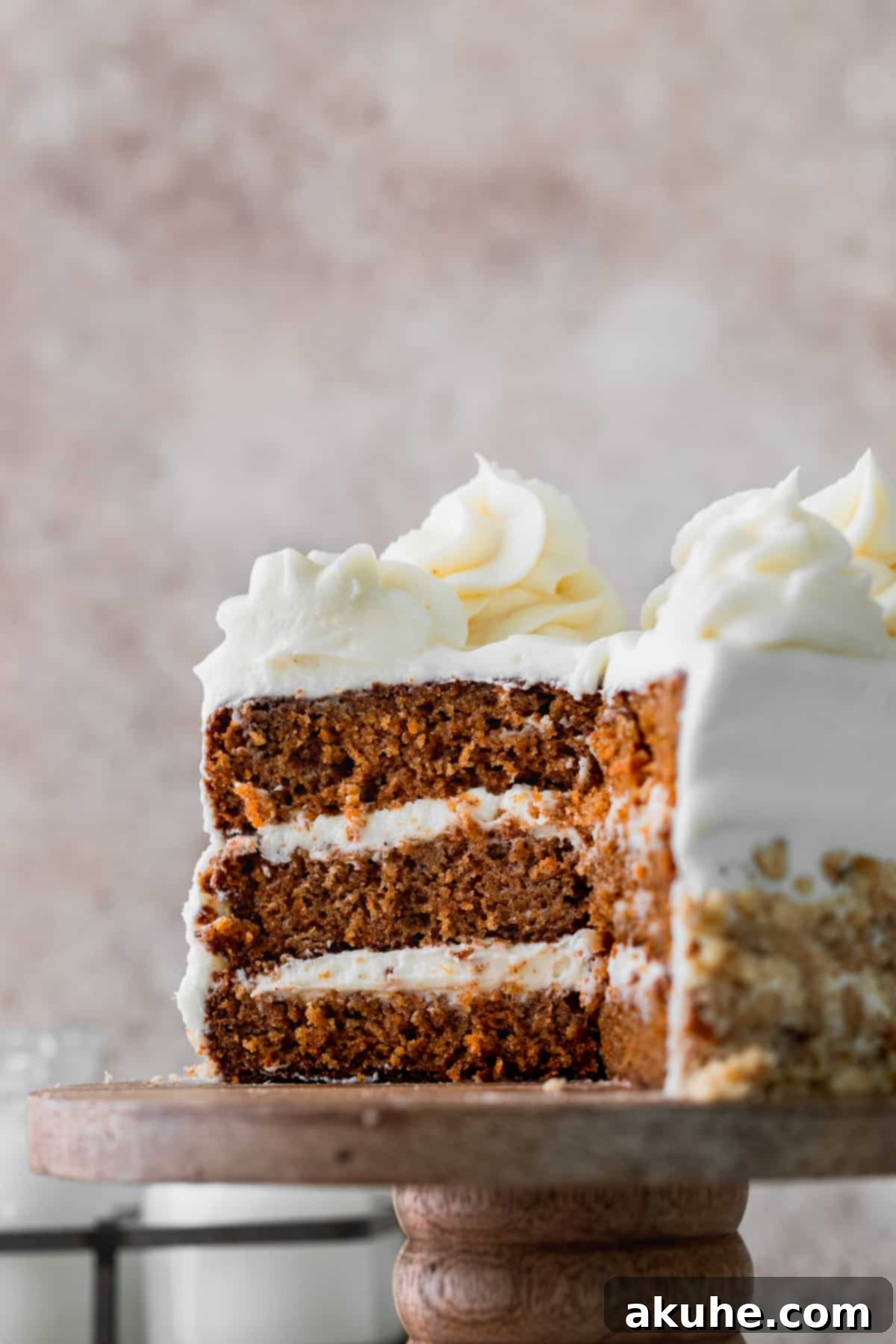 A mini carrot cake with a slice cut out, showcasing its layers and frosting, on a cake stand.
