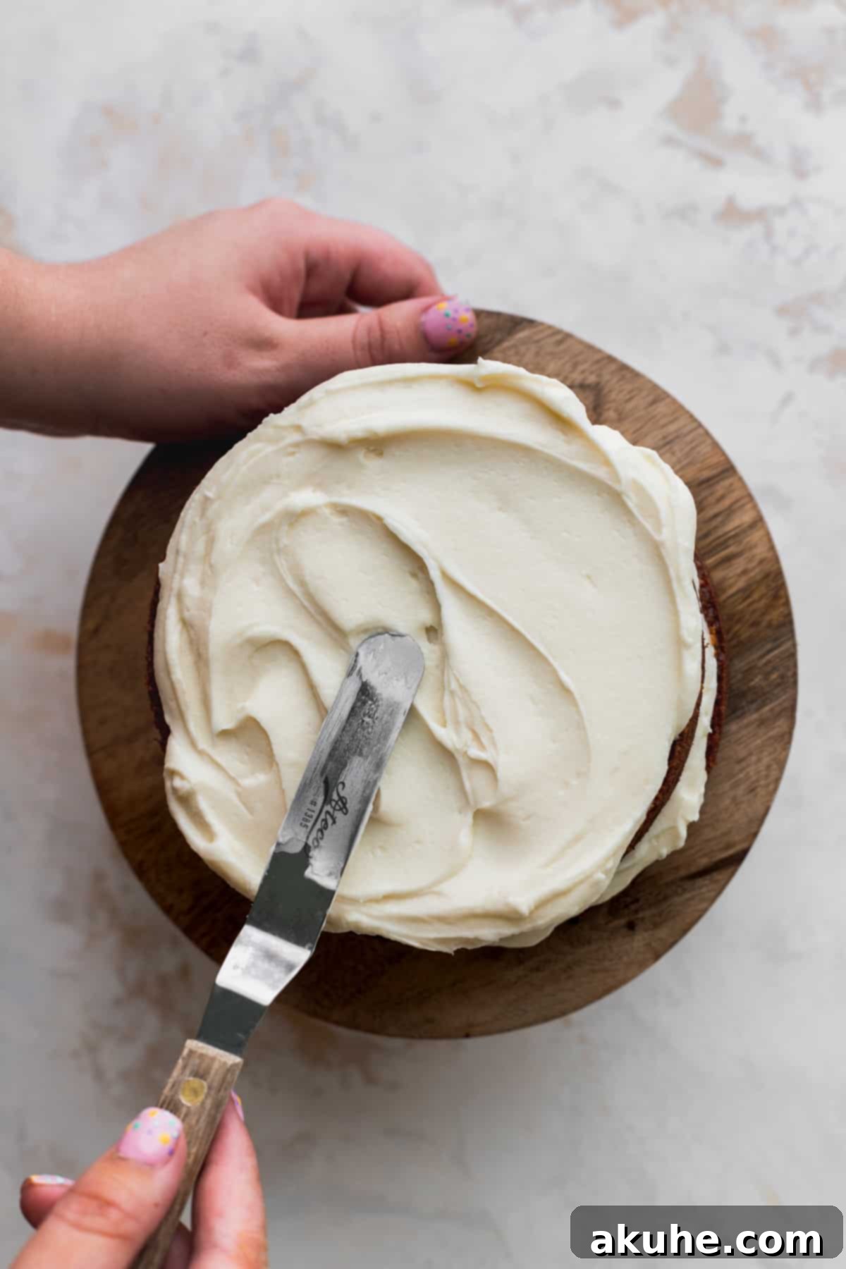 Applying a crumb coat of cream cheese frosting to a mini carrot cake.