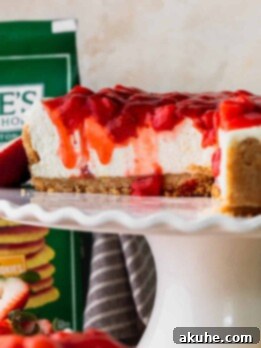 Lemon cheesecake with strawberry sauce cut into on a cake stand.