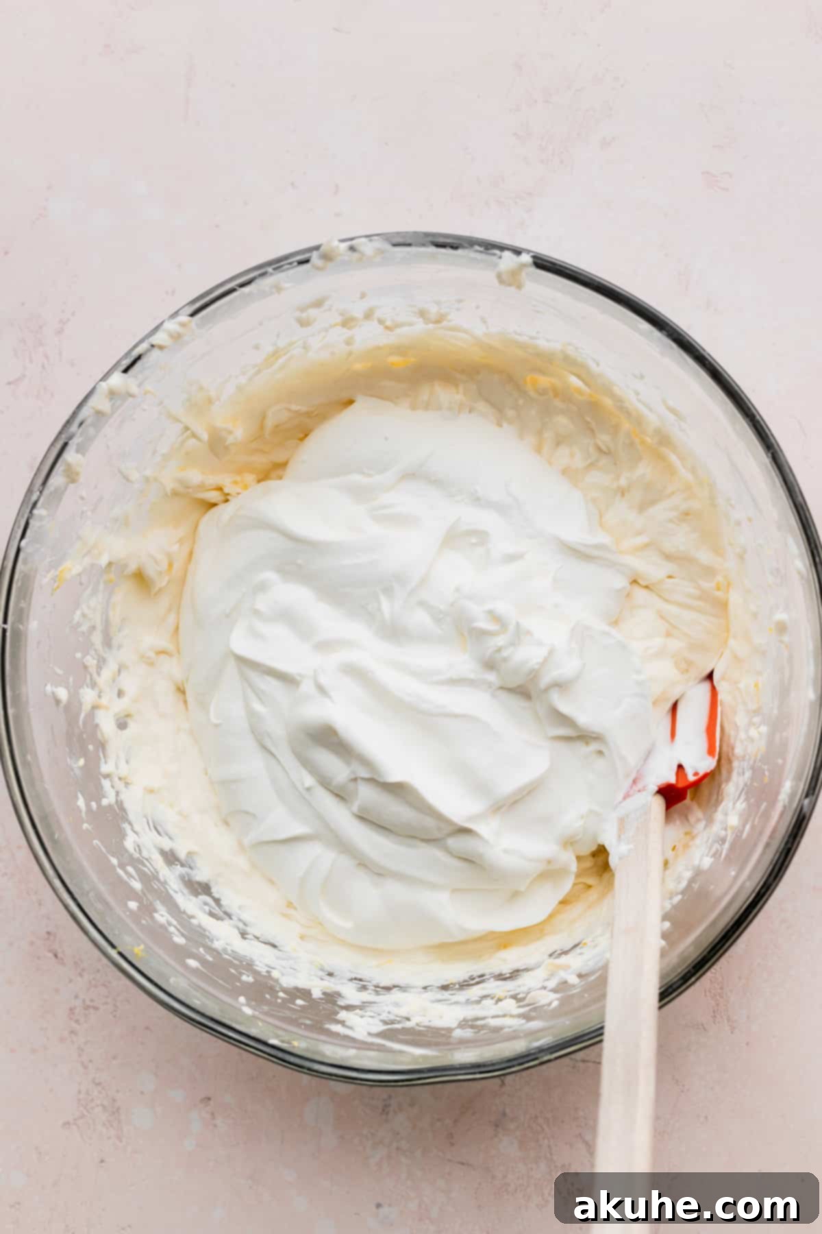 Whipped cream on top of cream cheese mixture in a glass bowl.