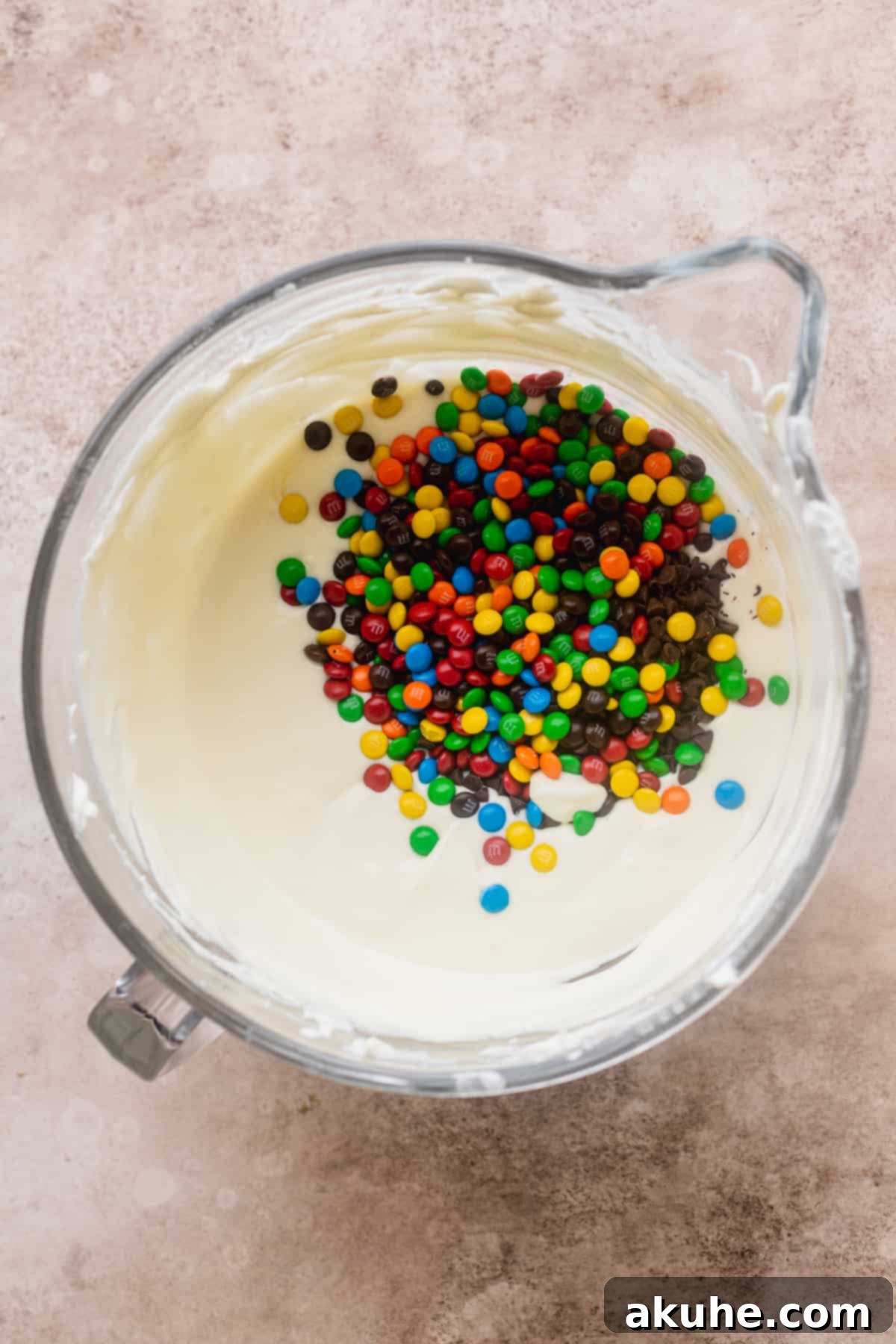 Vibrant mini M&M's scattered atop the smooth cheesecake batter, promising colorful bites.