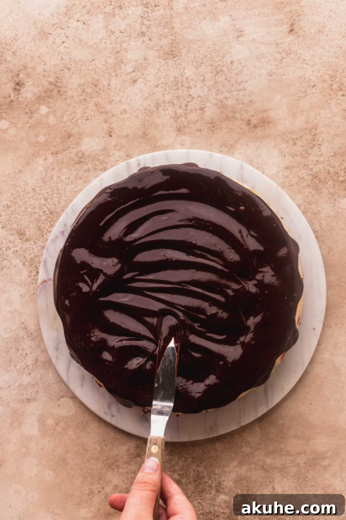 Smooth chocolate ganache being carefully spread over the chilled cheesecake, creating a glossy, rich layer.