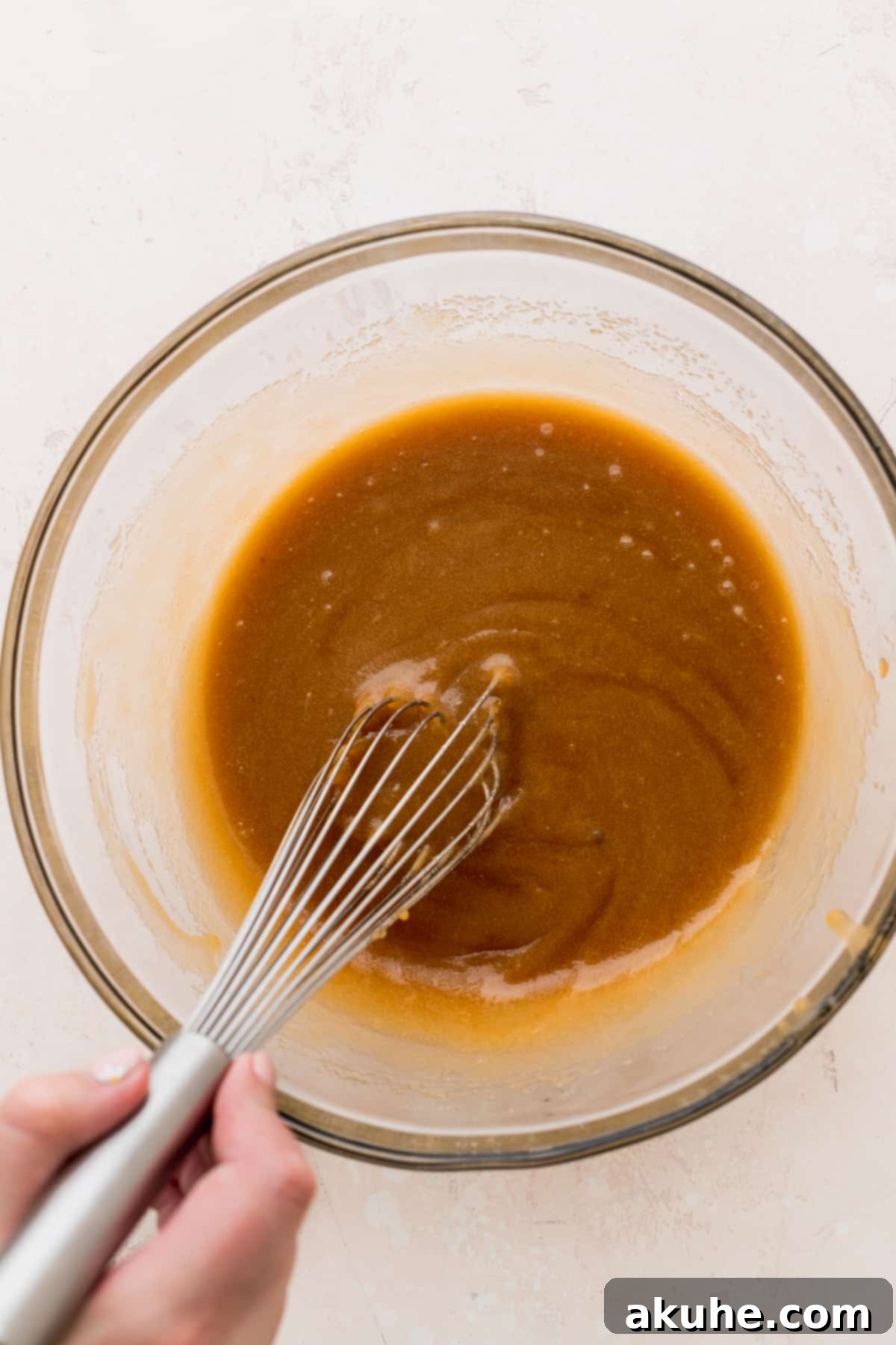 Wet ingredients being mixed in a clear glass bowl, showcasing a smooth, creamy texture.