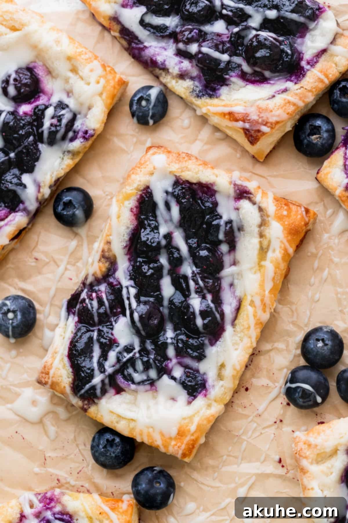 Close up of blueberry danish on parchment paper, highlighting its flaky layers and rich filling.