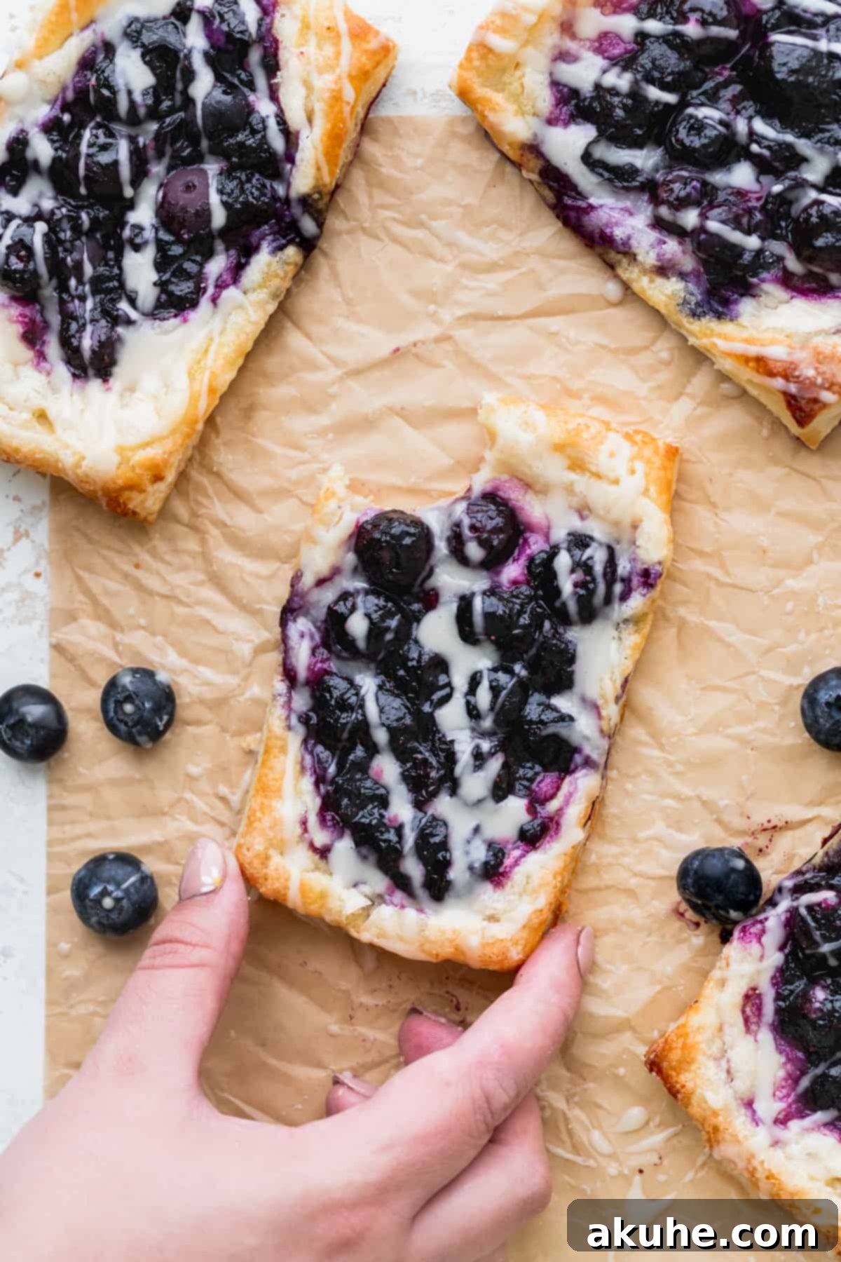 A hand taking a bite from a blueberry danish, showing the delicious filling.