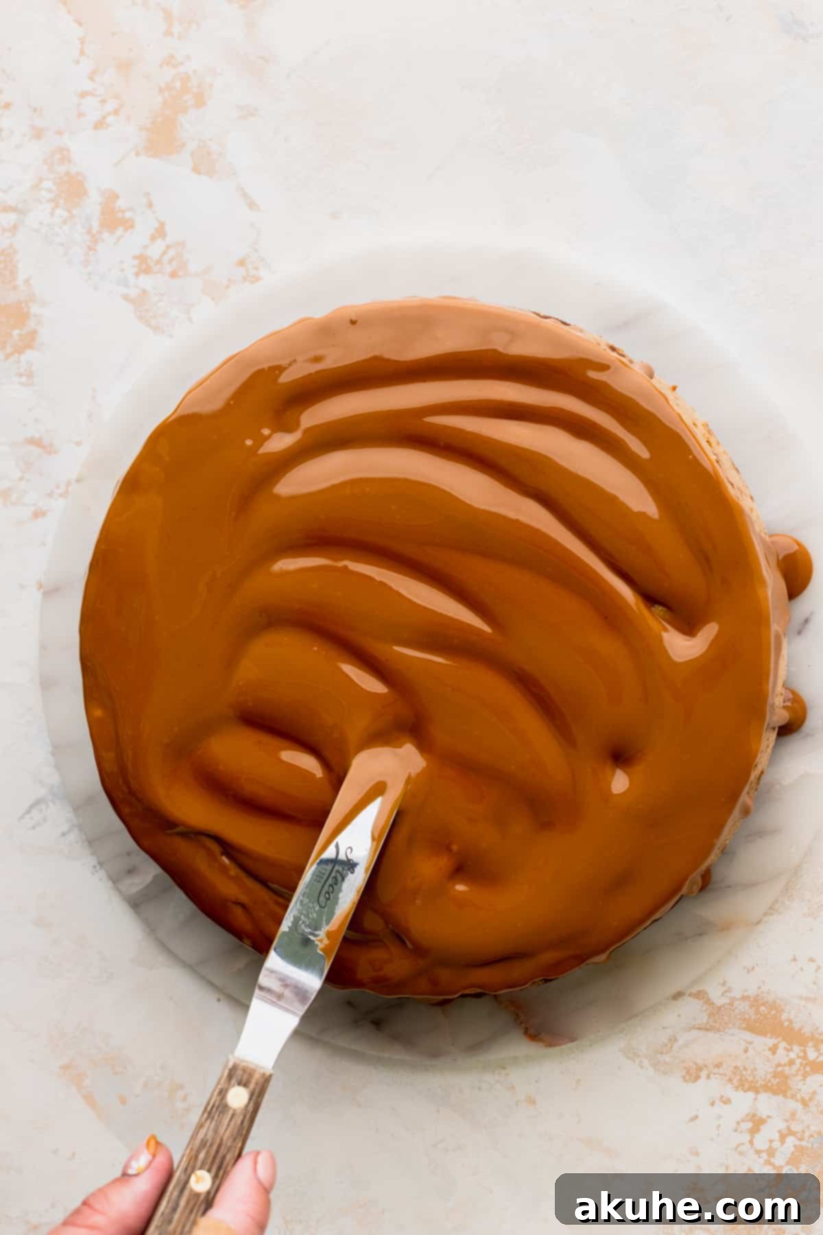 The Ultimate Biscoff Cheesecake 11 Delicious Biscoff cookie butter being spread and drizzled over the top of a creamy cheesecake, creating an appealing glaze.