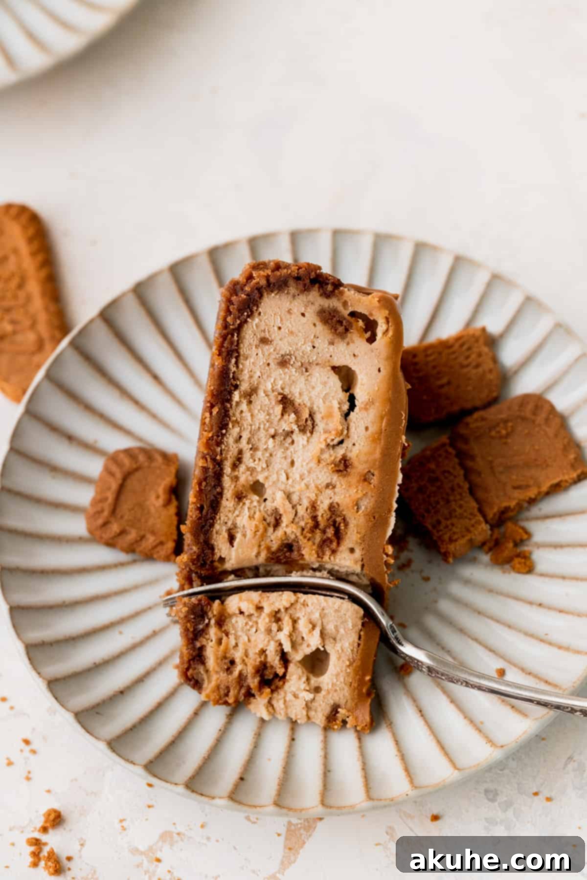 The Ultimate Biscoff Cheesecake 3 A perfectly sliced piece of Biscoff cheesecake on a white plate, highlighting its creamy texture and crunchy cookie bits.