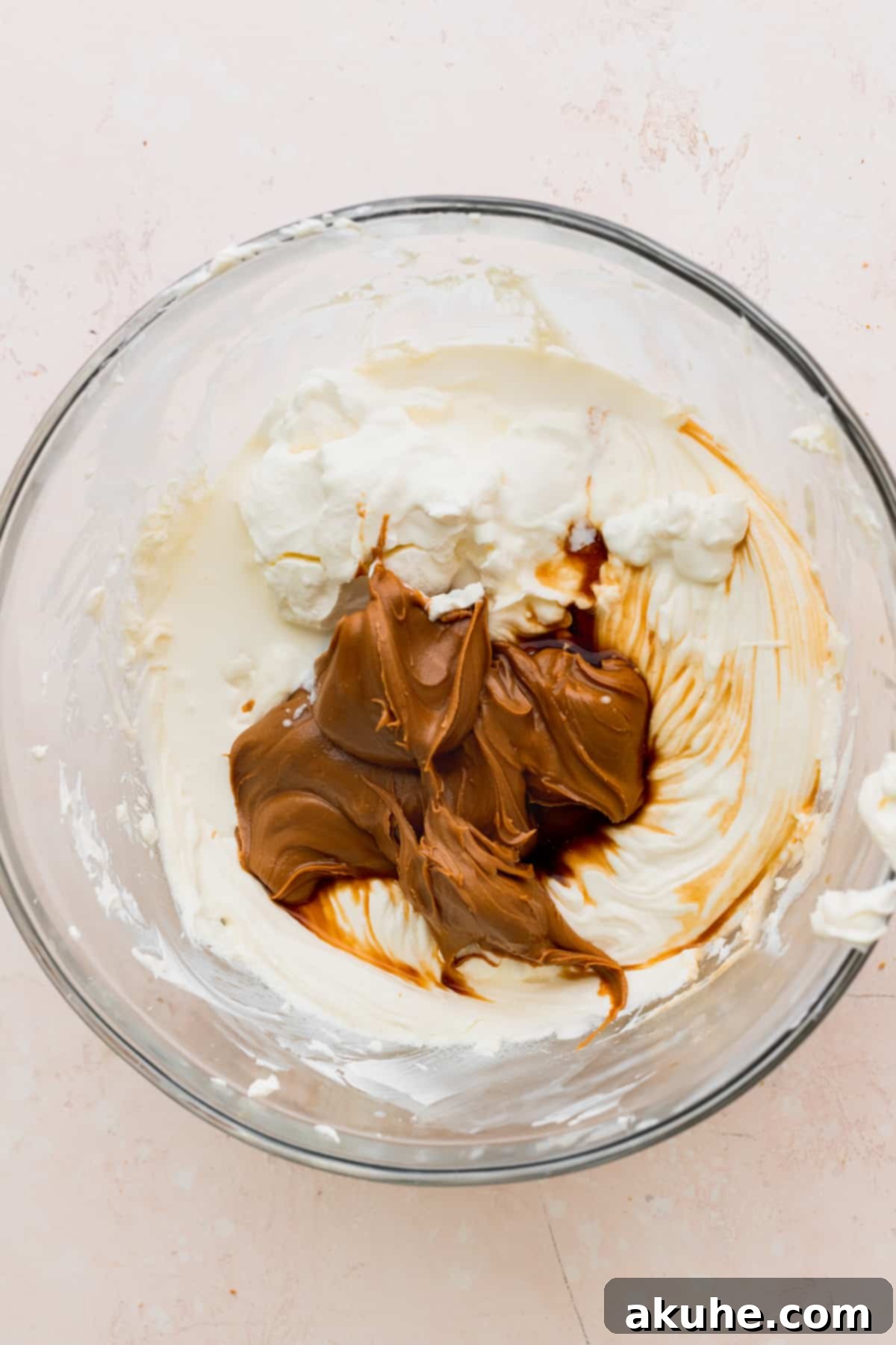 The Ultimate Biscoff Cheesecake 6 Smooth Biscoff cookie butter being added to the creamy cream cheese mixture in a glass bowl.