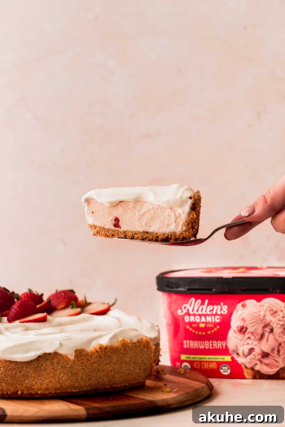 Taking one slice out of the strawberry ice cream cheesecake, revealing its creamy texture and vibrant strawberry specks.