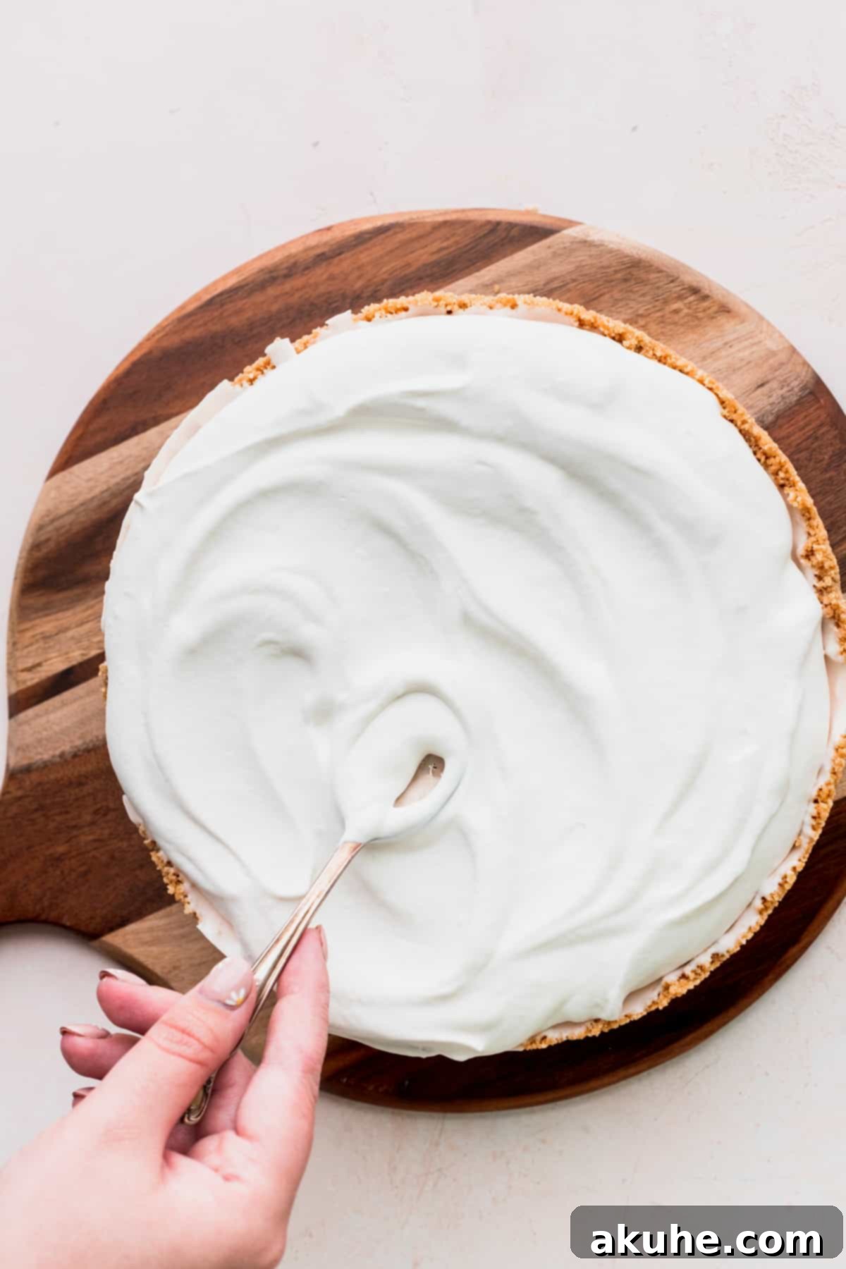 Spreading smooth, white whipped cream on top of the frozen strawberry ice cream cheesecake.