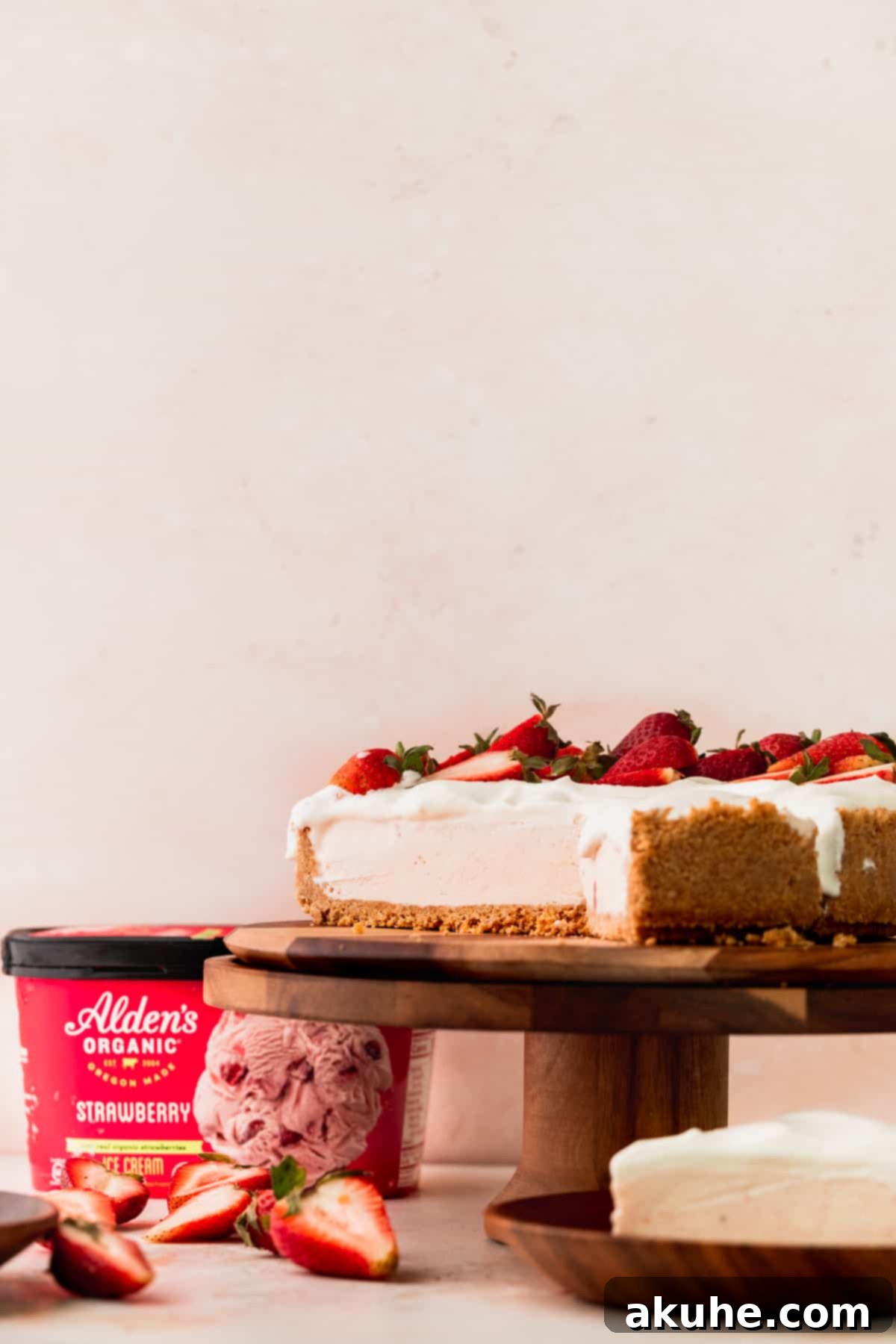 A strawberry ice cream cheesecake on a cake stand with several slices already removed, showing the inner layers.