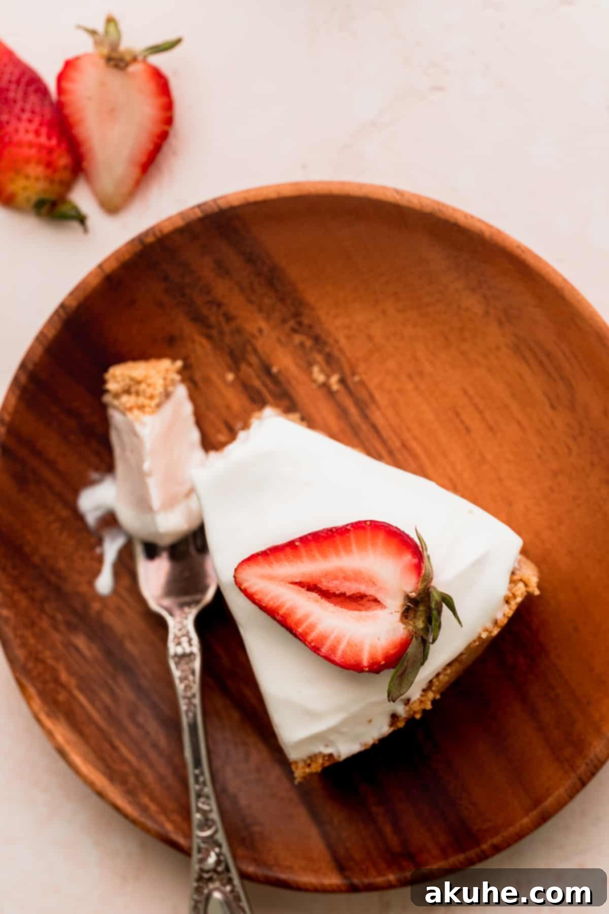 A beautiful top-down view of a single slice of strawberry ice cream cheesecake on a white plate, garnished with a fresh strawberry.