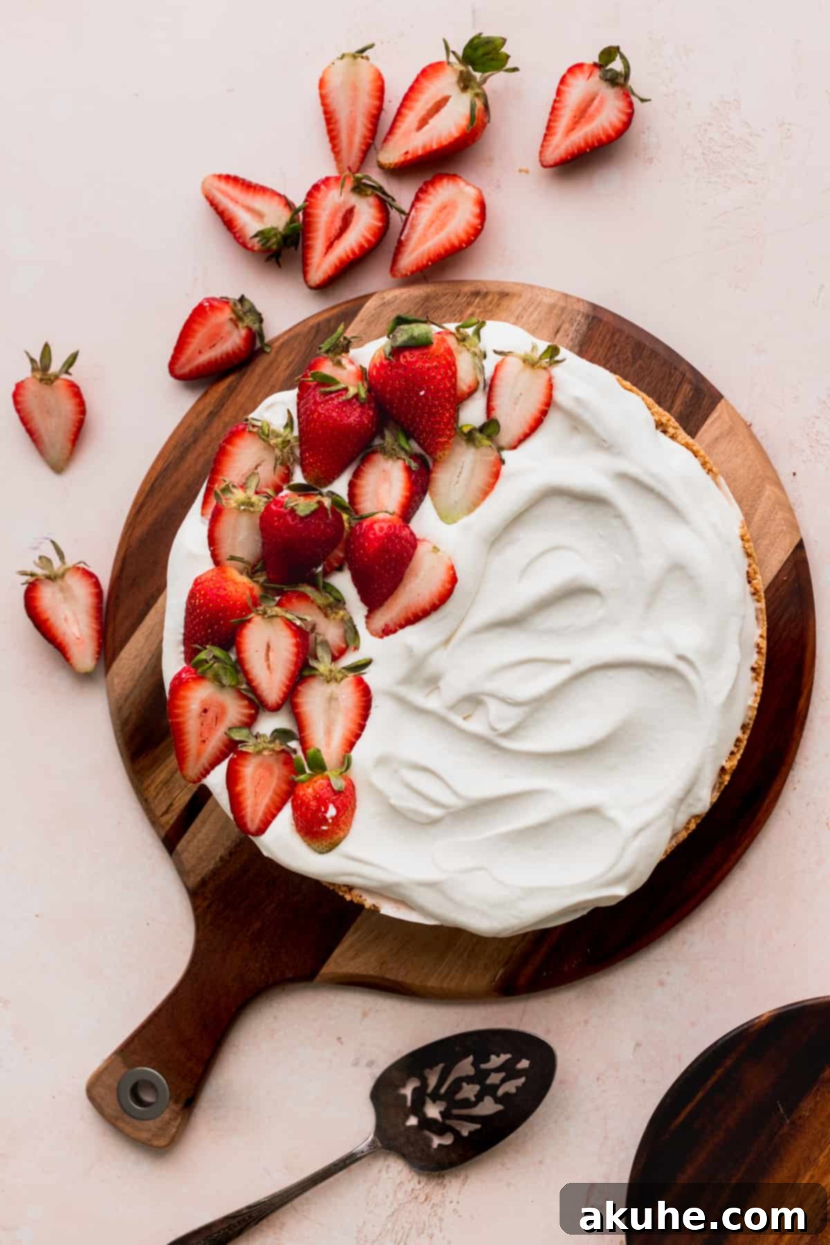 Cheesecake on a wooden platter with glistening fresh strawberries on top, ready to be served.