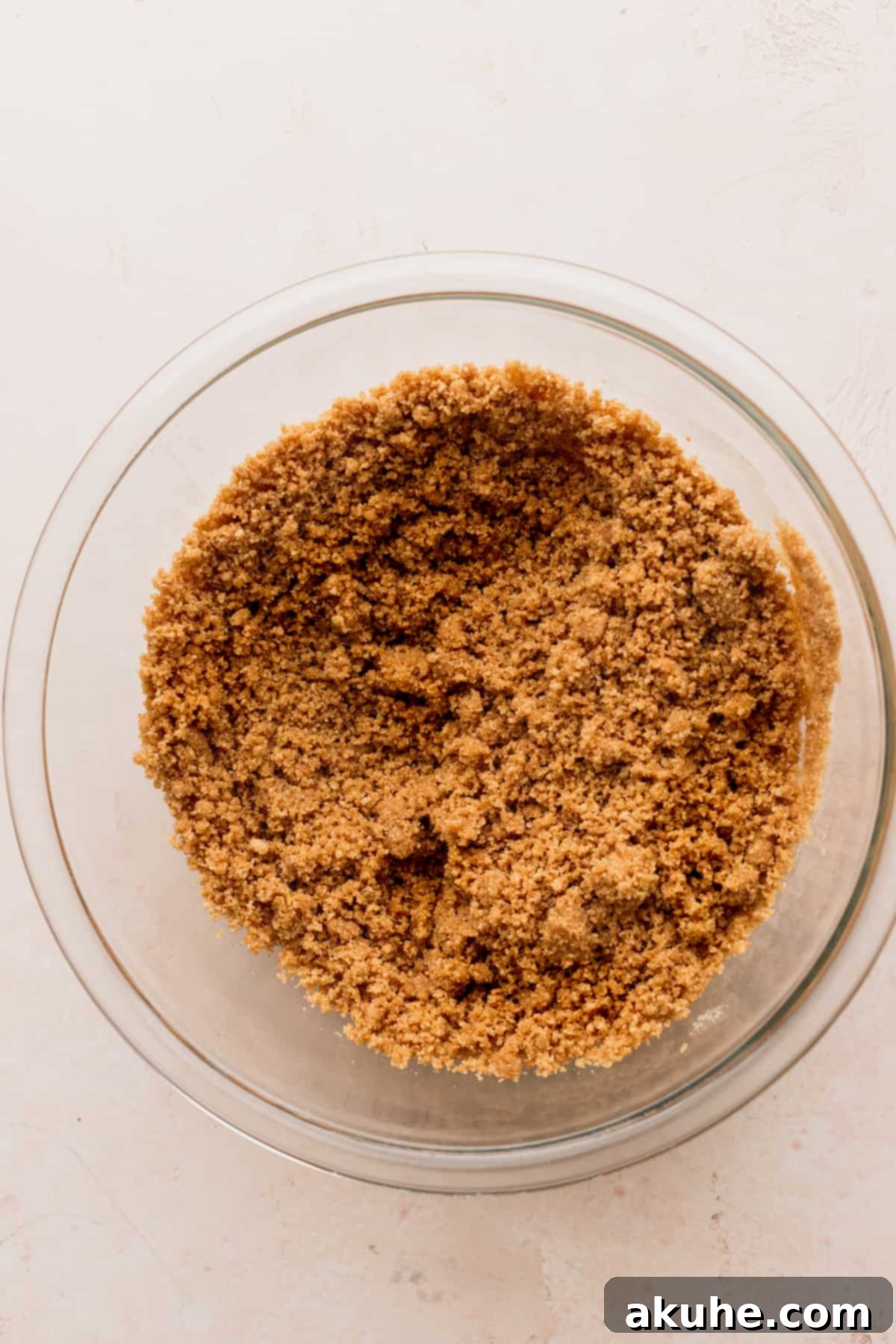 Close-up of graham cracker crumbs mixed with butter in a glass bowl.