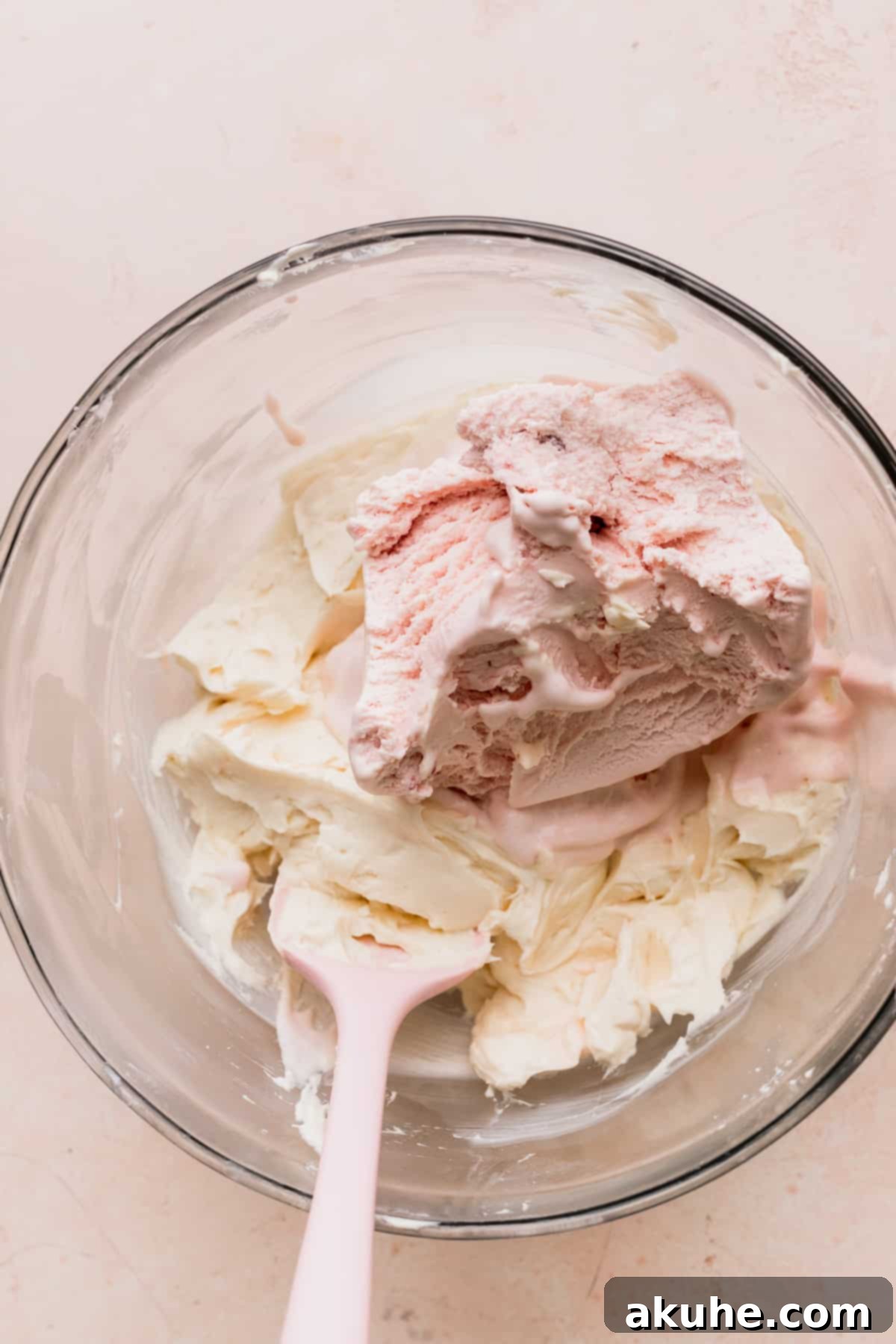 Softened strawberry ice cream scooped on top of the cream cheese mixture in a glass bowl.