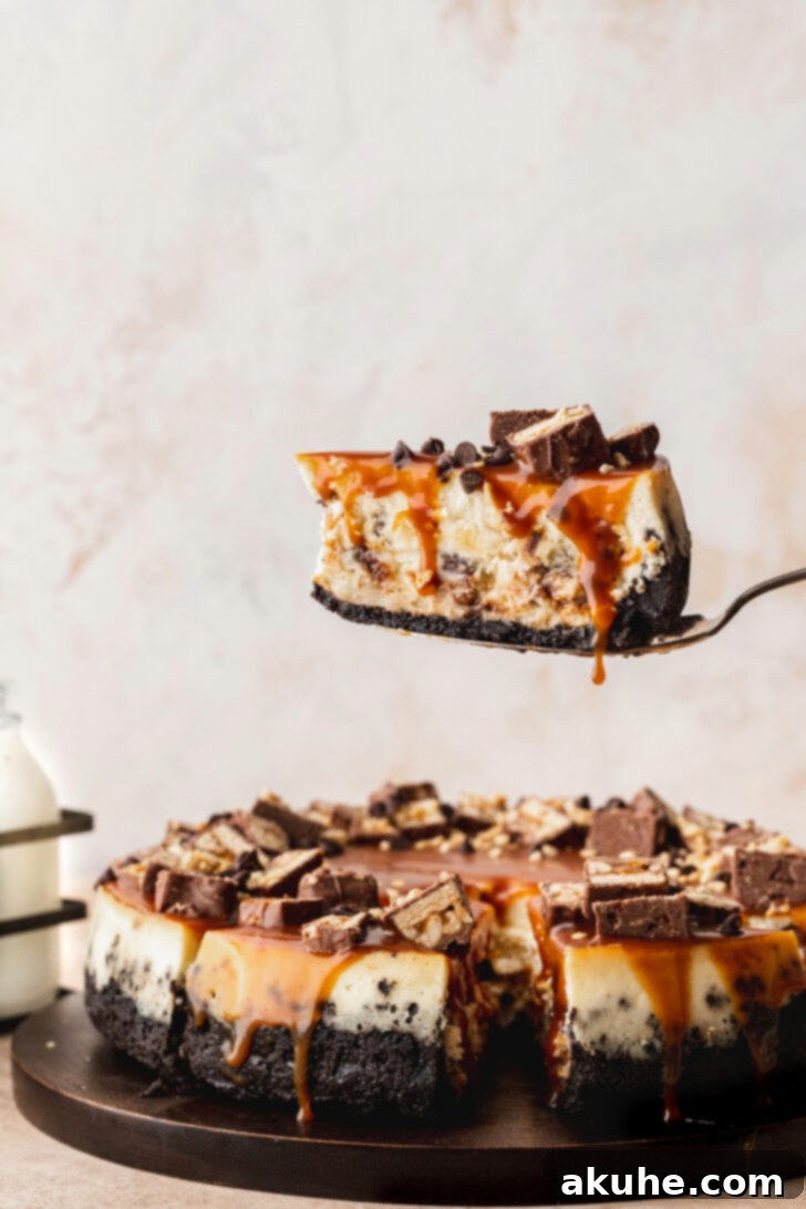 Snickers Bar Cheesecake Perfection 3 A hand gently removing a pristine slice from a freshly baked Snickers cheesecake, revealing the rich interior.