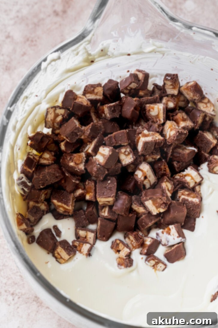 Snickers Bar Cheesecake Perfection 4 Chopped Snickers candy bars sprinkled evenly over the creamy cheesecake batter in a springform pan.