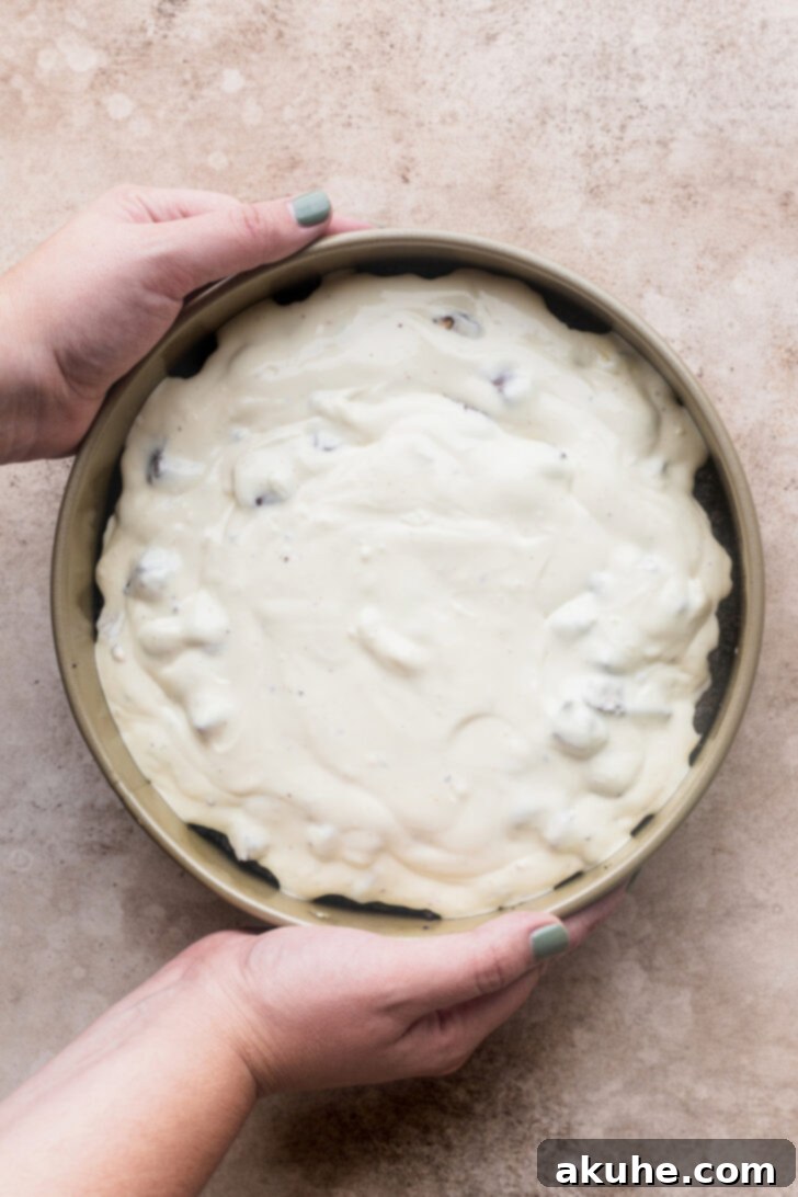 Snickers Bar Cheesecake Perfection 5 Smooth, unbaked cheesecake batter, rich with Snickers pieces, settling into a pre-baked Oreo crust.