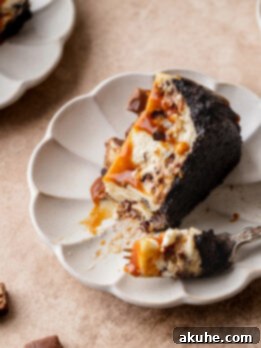 Snickers Bar Cheesecake Perfection 10 A slice of Snickers cheesecake on its side on a plate.