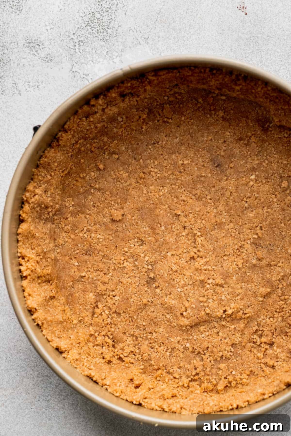 A meticulously pressed graham cracker crust lining the base and sides of a springform pan, ready for the creamy filling.