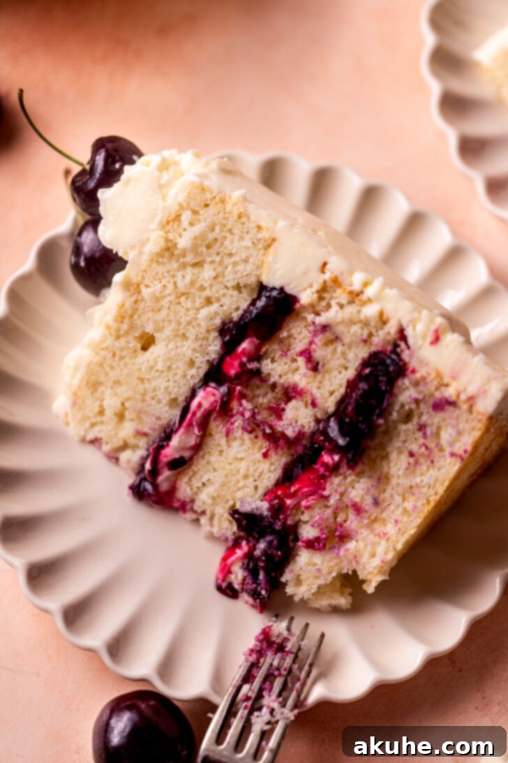 A perfectly sliced piece of homemade White Forest Cake on a elegant white plate, showcasing its three layers of fluffy white cake, vibrant cherry filling, and smooth white chocolate frosting, ready to be enjoyed.