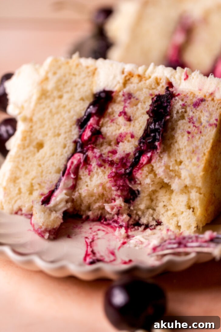 A close-up of a slice of White Forest Cake, showing the moist white cake, juicy cherry layers, and creamy white chocolate frosting in detail.