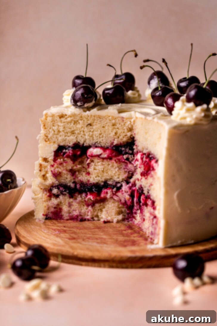 A full side profile view of a beautifully frosted White Forest Cake, elegantly presented on a rustic wooden board, highlighting its towering layers and smooth finish.