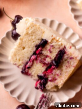 A slice of white forest cake on a plate, showcasing its layers of white cake, cherry filling, and white chocolate frosting.