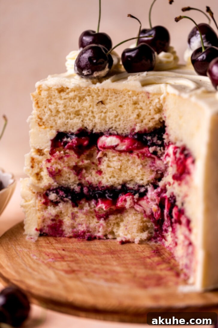 A close-up side view of a layered White Forest Cake, showcasing the distinct layers of white cake, a thick cherry filling, and generous white chocolate frosting, with a smooth, pristine finish.