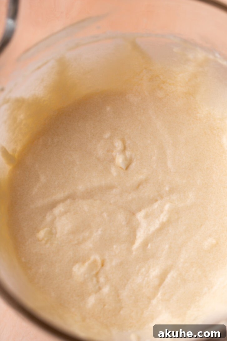 A mixing bowl filled with wet cake ingredients, including sour cream, vanilla extract, and egg whites, demonstrating their creamy consistency before being combined with dry ingredients.