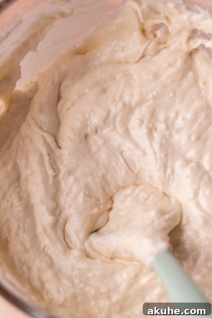 A close-up of smooth, thick white cake batter in a mixing bowl, showcasing its easily spreadable texture, ready for portioning into cake pans.