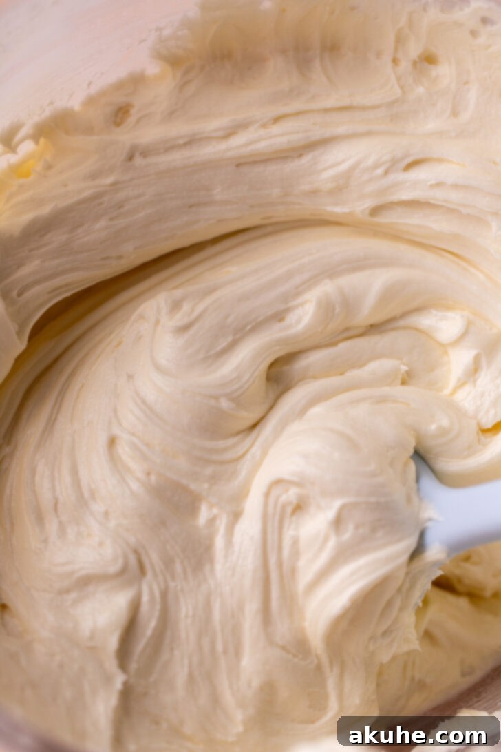 A bowl of creamy, off-white white chocolate frosting, showing its slightly looser but still pipeable consistency, ready for cake decoration.