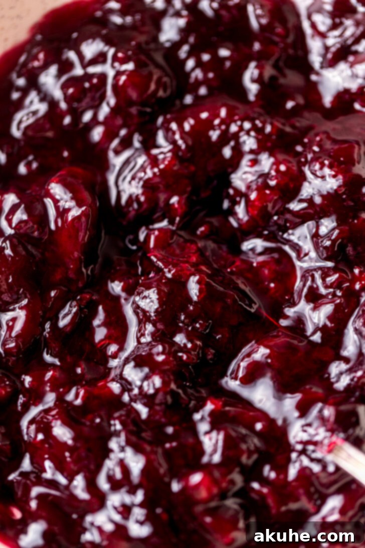 A close-up view of a bowl filled with vibrant red cherry pie filling, showcasing the chunky texture of the fruit, emphasizing that it needs to cool down before use.