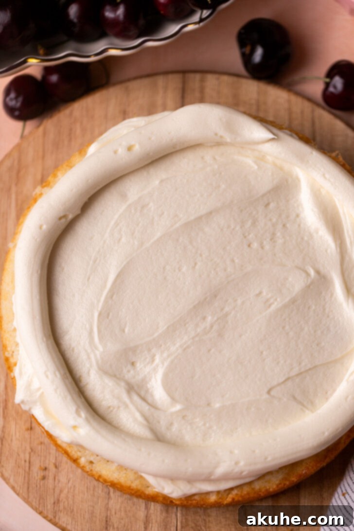 A cake layer partially covered with white frosting, with a piped border of frosting creating a well to contain the cherry filling.