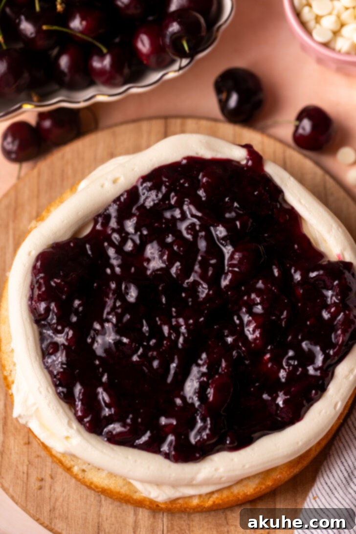 Vibrant cherry pie filling spread evenly within the piped frosting border on a cake layer, ready for the next cake layer to be placed on top.
