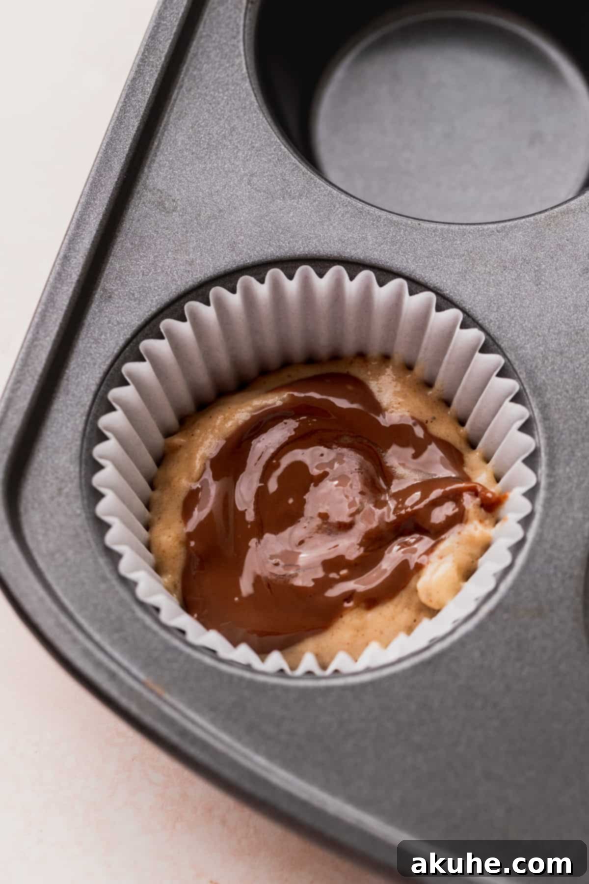 Nutella Swirl Banana Muffins 7 Muffin liners half-filled with banana batter, each topped with a dollop of melted Nutella.