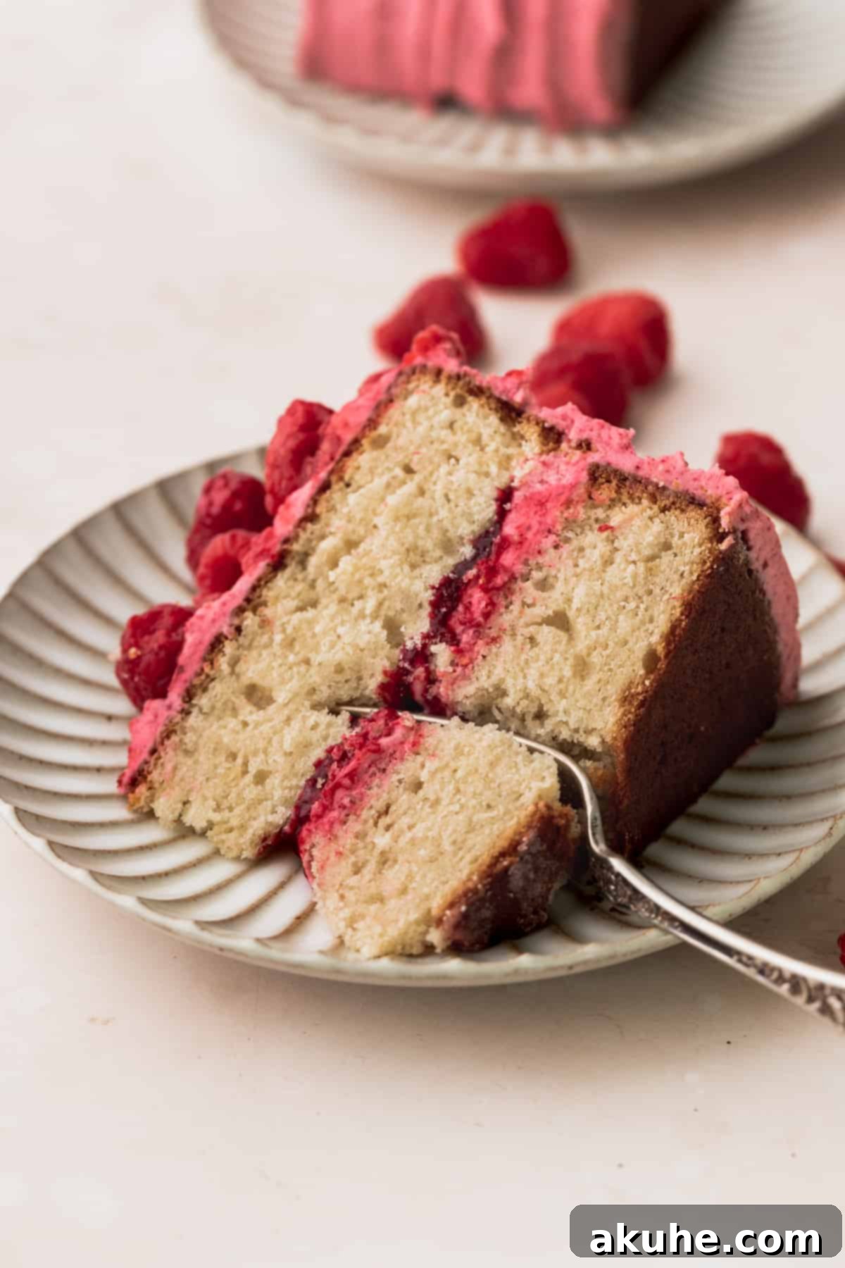 A single, perfectly sliced piece of vanilla raspberry cake, showcasing its beautiful layers of moist vanilla cake, vibrant raspberry jam, and creamy raspberry frosting, presented on a white plate.