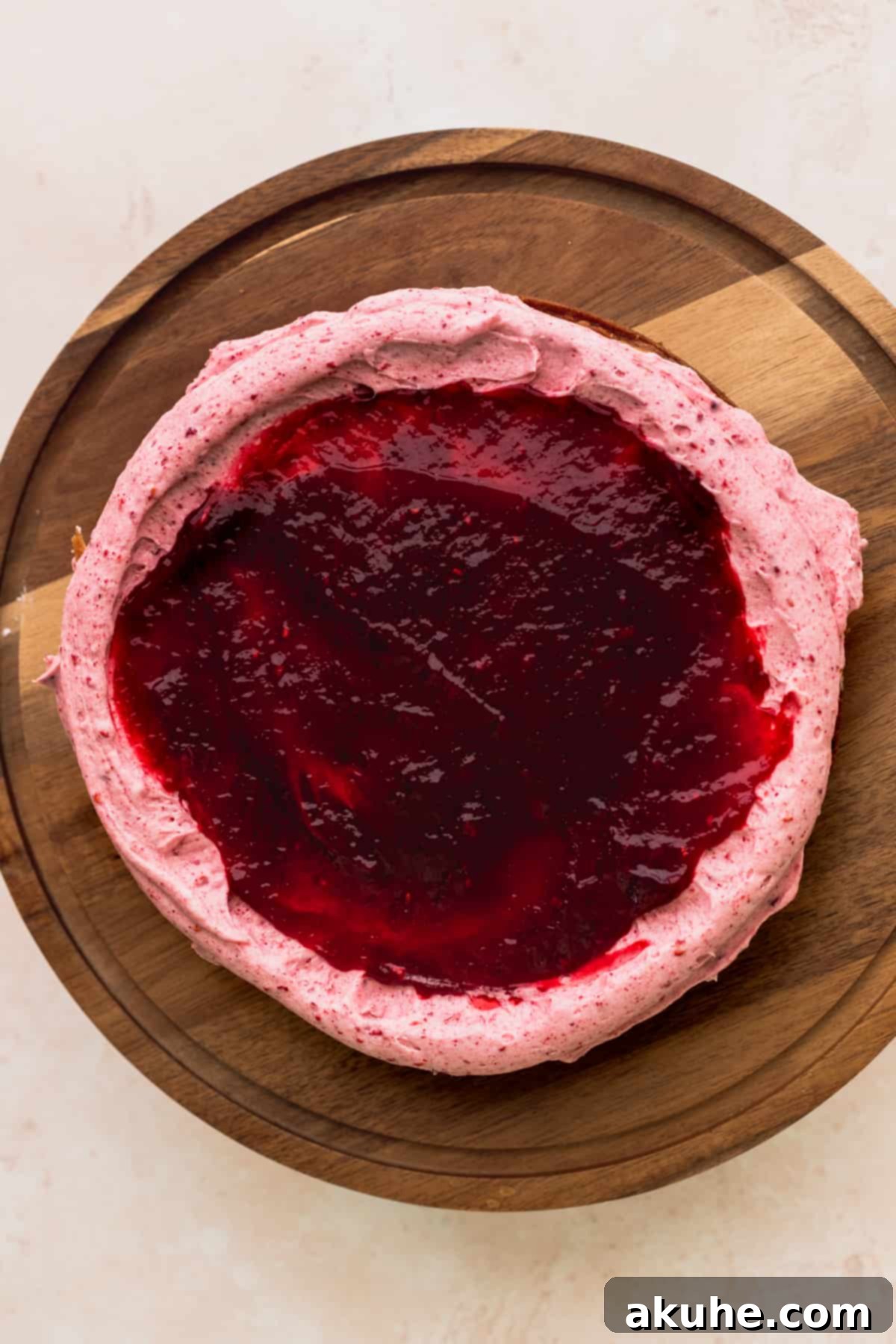 A generous layer of vibrant raspberry jam carefully spread over the first vanilla cake layer, contained by a piped frosting border, ready for the top cake layer.