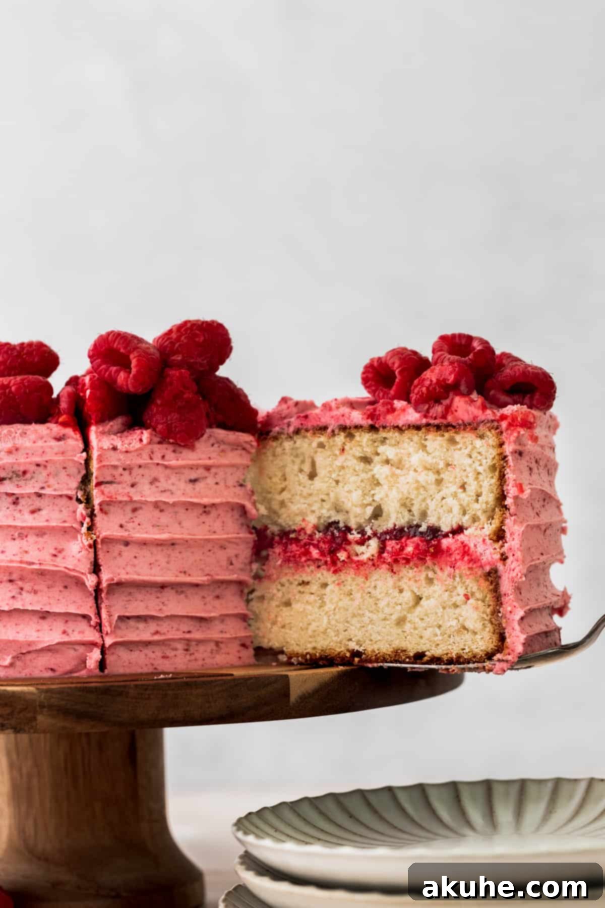 A hand gently removing a perfect slice of vanilla raspberry cake from the main cake, revealing its beautiful layers.
